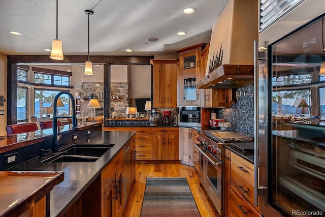 kitchen featuring wall chimney range hood, pendant lighting, double oven range, sink, and wall oven