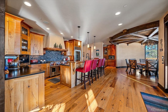 kitchen featuring decorative light fixtures, light hardwood / wood-style floors, custom exhaust hood, premium appliances, and a kitchen breakfast bar