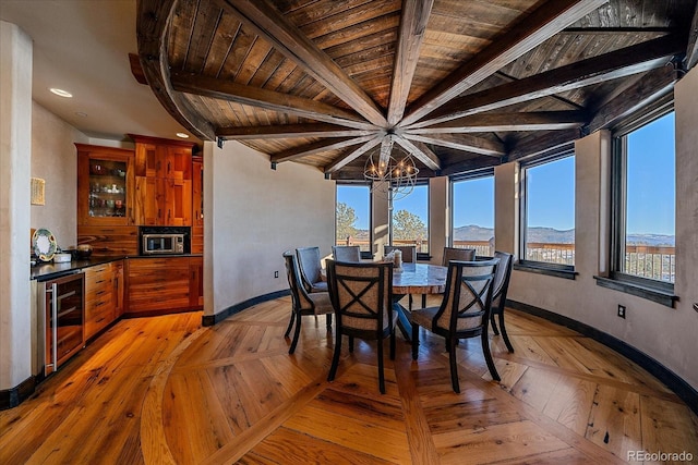 dining area with wood ceiling, a mountain view, a notable chandelier, wine cooler, and beam ceiling