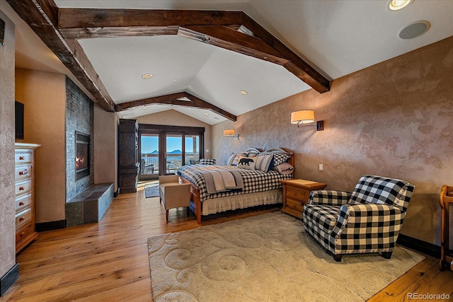 bedroom featuring light hardwood / wood-style flooring, a tiled fireplace, and vaulted ceiling with beams