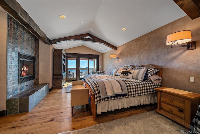 bedroom featuring vaulted ceiling with beams, a fireplace, and light hardwood / wood-style flooring