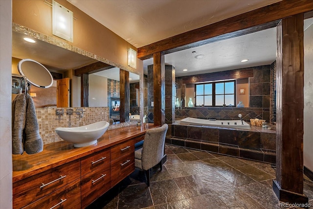 bathroom featuring decorative backsplash, tiled tub, and vanity