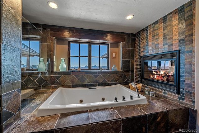 bathroom featuring tile walls, a fireplace, and a relaxing tiled tub