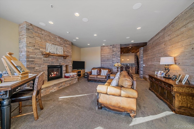 living room with wood walls, a stone fireplace, and carpet flooring