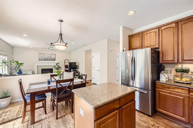 3744 Gypsum Ct, Superior, CO 80027 - kitchen featuring freestanding refrigerator, a kitchen island, ceiling fan, a tile fireplace, and light wood-style flooring