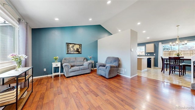 living room with a notable chandelier, visible vents, baseboards, vaulted ceiling, and light wood-type flooring