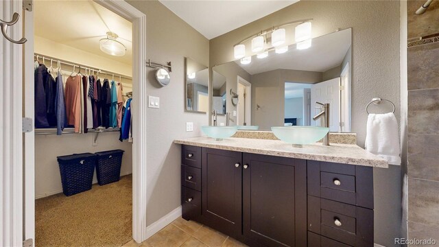 bathroom with tile patterned flooring, a spacious closet, baseboards, and vanity