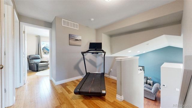 exercise area with light wood-style floors, lofted ceiling, visible vents, and baseboards