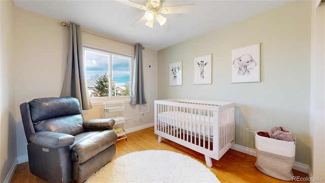 bedroom featuring a nursery area, ceiling fan, baseboards, and wood finished floors