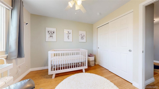 bedroom with a crib, baseboards, a ceiling fan, light wood-type flooring, and a closet