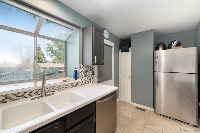 kitchen with stainless steel appliances, a sink, tasteful backsplash, light tile patterned floors, and light countertops