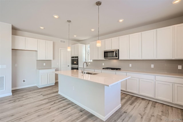 kitchen featuring pendant lighting, a kitchen island with sink, white cabinets, sink, and stainless steel appliances