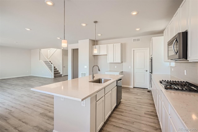 kitchen featuring sink, hanging light fixtures, a center island with sink, white cabinets, and appliances with stainless steel finishes