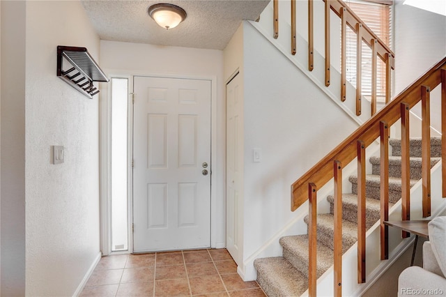 foyer with baseboards, stairway, light tile patterned floors, and a textured ceiling
