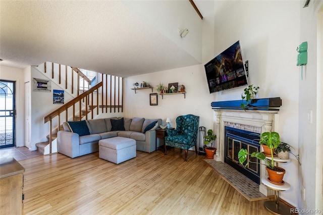 living room with stairway, wood finished floors, a glass covered fireplace, a textured ceiling, and baseboards