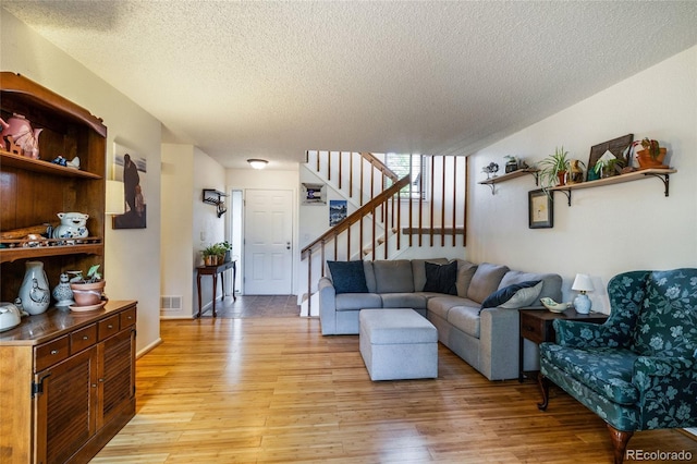 living area featuring a textured ceiling, light wood finished floors, and stairs