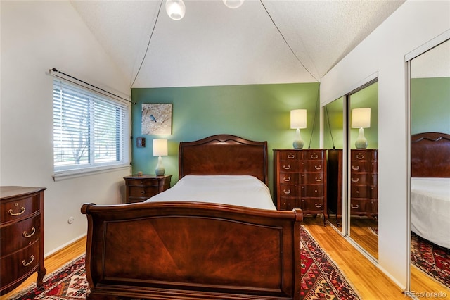 bedroom with wood finished floors, multiple closets, and lofted ceiling