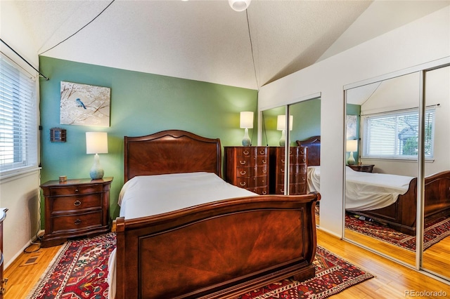 bedroom featuring multiple windows, vaulted ceiling, wood finished floors, and multiple closets