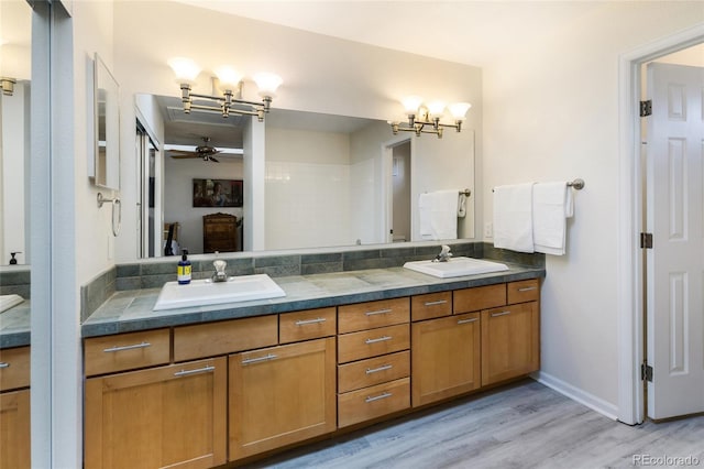 bathroom featuring ceiling fan, wood finished floors, double vanity, a chandelier, and baseboards