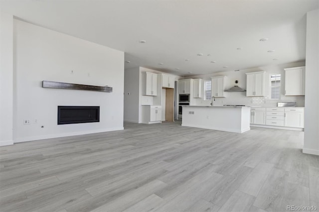 25234 E Warren Pl, Aurora, CO 80018 - unfurnished living room featuring light wood-style flooring, a glass covered fireplace, a sink, baseboards, and recessed lighting