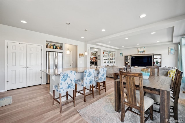 dining space featuring recessed lighting, a raised ceiling, and light wood-type flooring