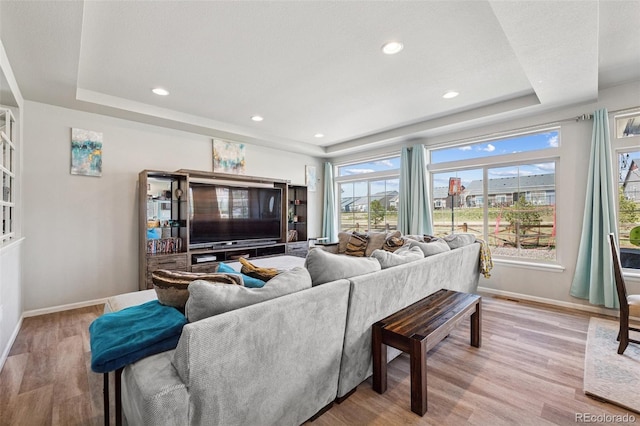 living room featuring light wood-style floors, baseboards, a tray ceiling, and recessed lighting