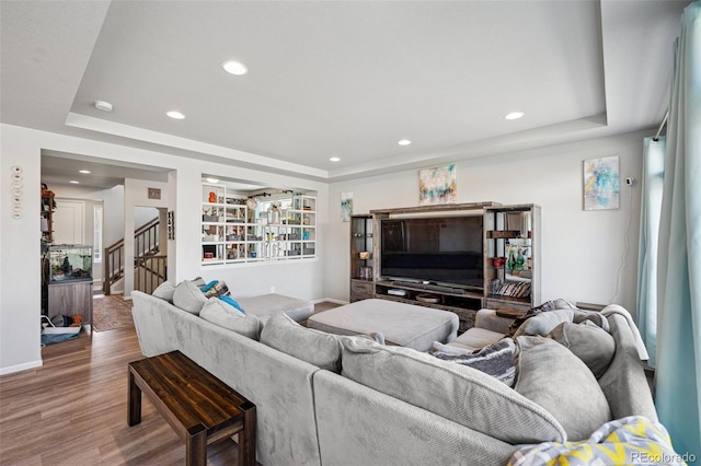 living room featuring recessed lighting, stairs, a raised ceiling, and wood finished floors