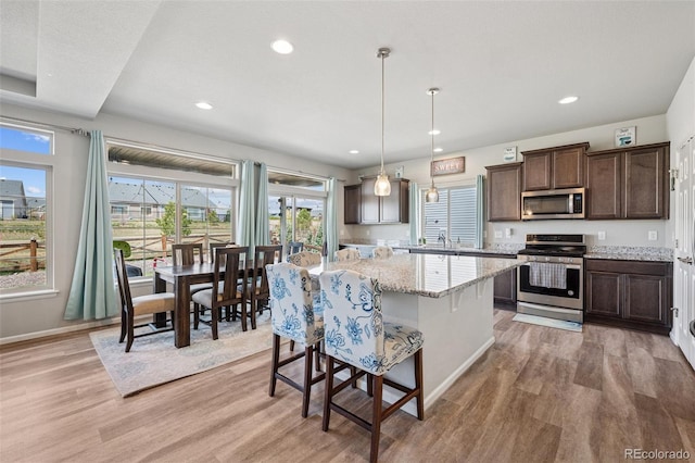 kitchen with dark brown cabinetry, a kitchen island, recessed lighting, light wood-style flooring, and stainless steel appliances