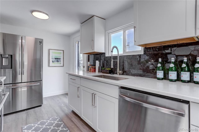 kitchen with light hardwood / wood-style flooring, stainless steel appliances, sink, decorative backsplash, and white cabinets