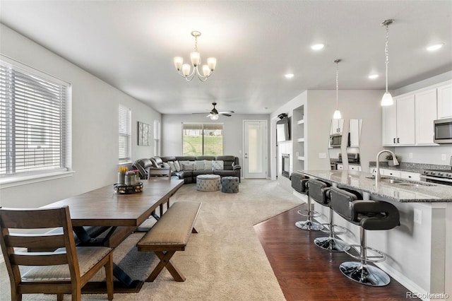 carpeted dining area with ceiling fan with notable chandelier and sink