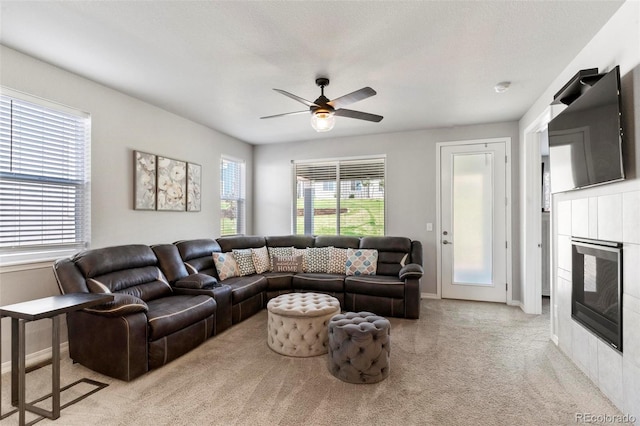 living room with light carpet, a textured ceiling, ceiling fan, and a tiled fireplace