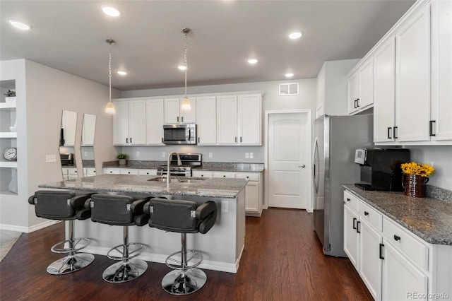 kitchen with appliances with stainless steel finishes, sink, pendant lighting, dark stone countertops, and white cabinetry