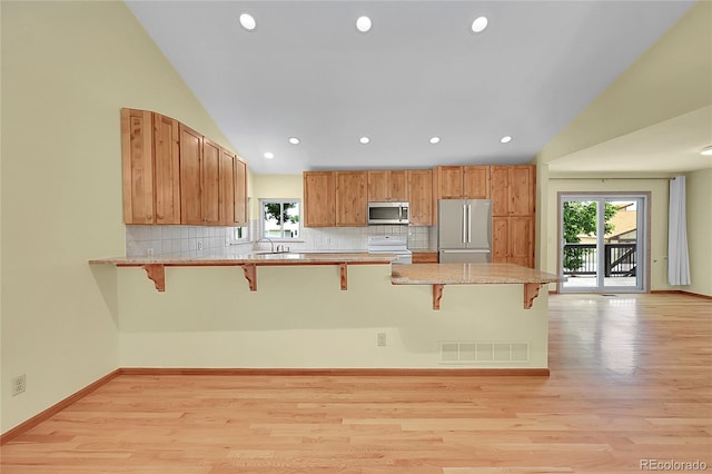1624 Daphne St, Broomfield, CO 80020 - kitchen featuring stainless steel appliances, a breakfast bar area, a peninsula, light wood-type flooring, and decorative backsplash