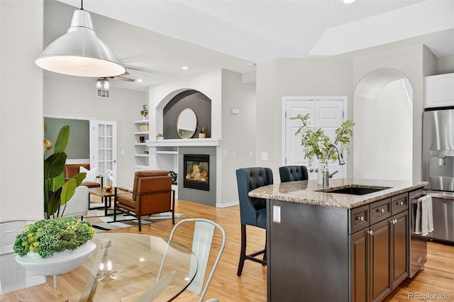 4501 Whitehall Ln, Highlands Ranch, CO 80126 - kitchen featuring appliances with stainless steel finishes, a breakfast bar area, light stone counters, light wood-type flooring, and a center island with sink
