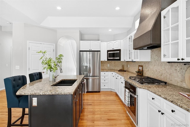 4501 Whitehall Ln, Highlands Ranch, CO 80126 - kitchen with stainless steel appliances, wall chimney exhaust hood, a breakfast bar, light wood-style floors, and white cabinets