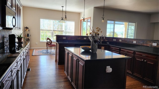 kitchen featuring dark wood-style flooring, decorative backsplash, a kitchen island with sink, a sink, and black appliances