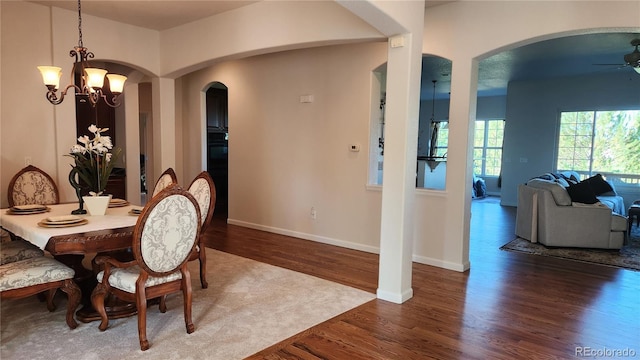 dining area with ceiling fan with notable chandelier, arched walkways, baseboards, and wood finished floors