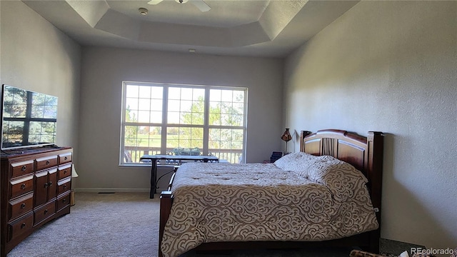 carpeted bedroom featuring a raised ceiling, ceiling fan, and baseboards