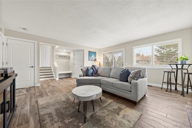 living room featuring a textured ceiling, stairway, wood finished floors, and baseboards