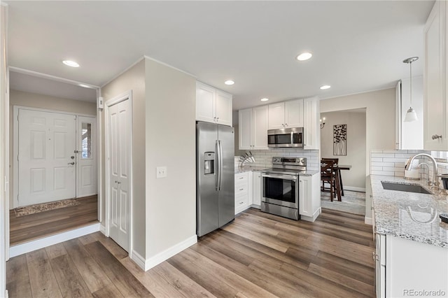 kitchen with light stone counters, appliances with stainless steel finishes, white cabinets, a sink, and wood finished floors