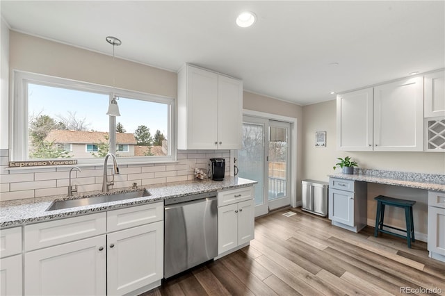 kitchen with tasteful backsplash, stainless steel dishwasher, white cabinetry, a sink, and wood finished floors