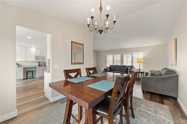 dining room featuring lofted ceiling, light wood finished floors, baseboards, and a chandelier