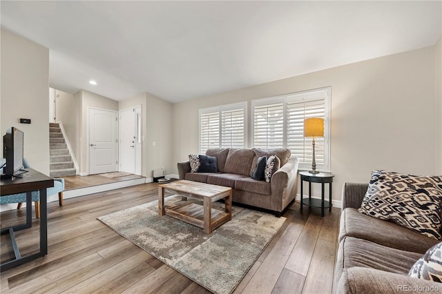 living area featuring light wood finished floors, stairs, baseboards, and vaulted ceiling