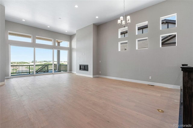 unfurnished living room featuring a towering ceiling, light hardwood / wood-style flooring, and a notable chandelier