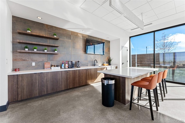 bar featuring sink, dark brown cabinets, and concrete flooring