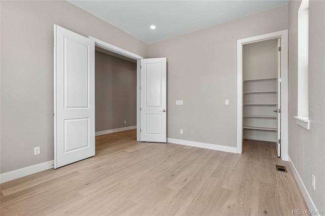 unfurnished bedroom with a closet, a spacious closet, and light hardwood / wood-style flooring