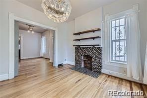 unfurnished living room with a tile fireplace, a chandelier, and light wood-type flooring