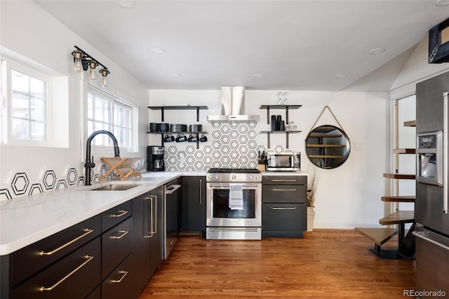 kitchen with wall chimney range hood, sink, hardwood / wood-style flooring, appliances with stainless steel finishes, and light stone counters