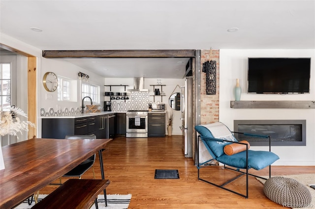 kitchen featuring light wood-type flooring, tasteful backsplash, wall chimney exhaust hood, stainless steel appliances, and sink