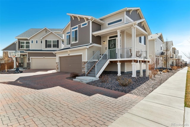 view of front of home with board and batten siding, covered porch, decorative driveway, stone siding, and an attached garage